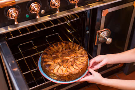 Hands take homemade apple pie out of the oven. Apple pie baking in oven. Traditional French apple pie in the oven.の写真素材