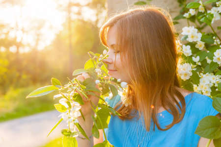 Portrait of beautiful blonde hair woman inhales the fragrance of spring flowers of blooming jasmine treeの写真素材
