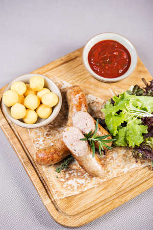 portion of tasty grilled homemade sausages with boiled potato, lettuce and savory tomato sauce on wooden boardの写真素材