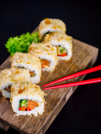 Katsuobushi Uramaki Sushi Roll with salmon and cucumber on wooden board on black background. Sushi roll with dry fish bonito flakesの写真素材