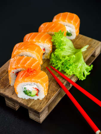 uramaki sushi roll with salmon, avocado, cream cheese philadelphia and tobiko flying fish caviar on black background with red chopsticksの写真素材