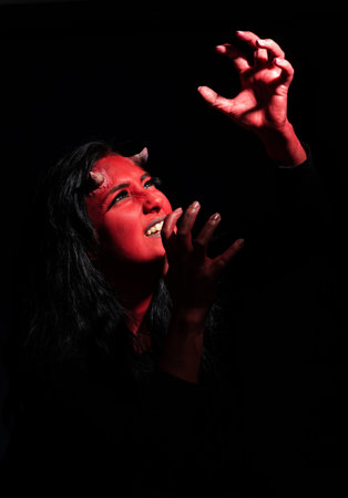 Screaming woman with long black hair and with face paint for halloween, demon woman with red face...