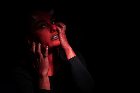Portrait of sexy woman with long black hair and with face paint for halloween, demon woman with red face and small horns on black background. Halloween concept. Halloween makeupの写真素材