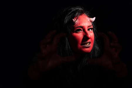 Portrait of sexy woman with long black hair and with face paint for halloween, demon woman with red face and small horns on black background. Halloween concept. Halloween makeupの写真素材
