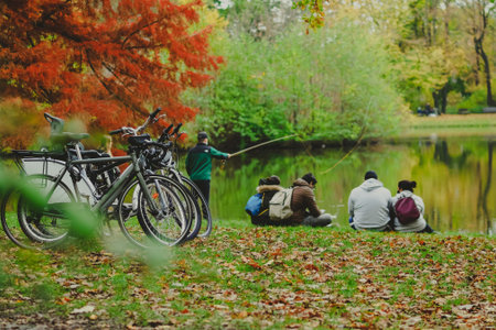 parked bicycles in autumn park and group of people near pond in city park in a rainy autumn day,...