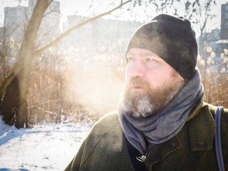 Man breathing in winter forest. Adult man wearing knit hat, breathing cold air. Bearded man relaxing...