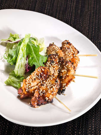portion of grilled chicken wings skewers with mix salad on a plate on dark backgroundの写真素材