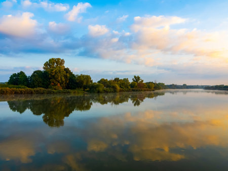 Morning sky with clouds over the river. Beautiful sunrise and reflecting clouds in a river. Nature landscape, reflection, blue and pink color sky, landscape during dawn.の写真素材