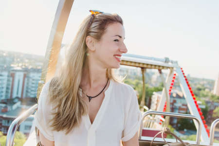 smiling young blond hair woman riding on ferris wheel looking on a city from above in a sunny summer dayの写真素材