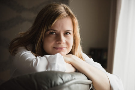 Happy smiling peaceful blond hair woman sitting on a couch at home. relaxing on sofa at home in the...