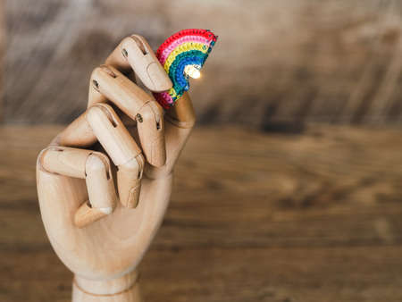 wooden hand of mannequin holding knitted rainbow on wooden background, close up on wooden background with copy spaceの写真素材