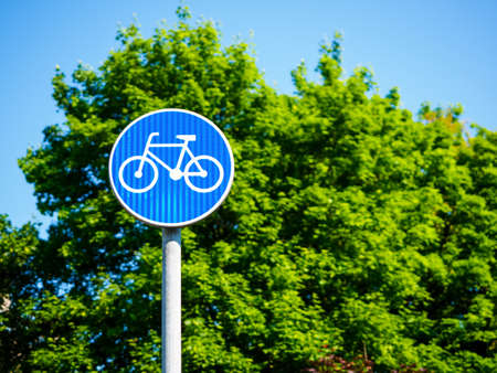 a blue bicycle sign sign signifying a bike path. bicycle lane, round blue road sign against green treeの写真素材