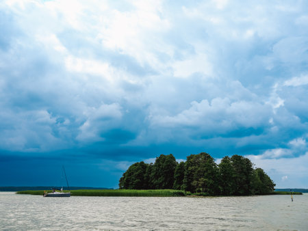 lonely island and moored small sailing yacht on a lake and dramatic cloudy sky on backgroundの写真素材