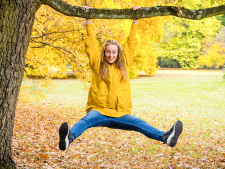 young funny pretty female hanging on a tree and having fun in autumn park in golden fall seasonの写真素材