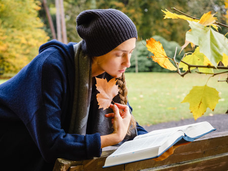 young pretty female reading a book outdoors in the city park in golden fall seasonの写真素材