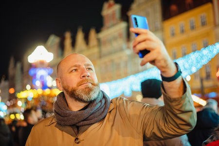Adult person take a photo by his smartphone on a city christmas fair. Man is taking selfie with smartphoneの写真素材