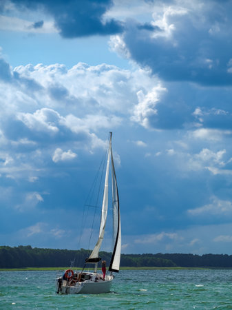 white sailboat sailing on a lake in a summer sunny day with clouds on a blue skyの写真素材