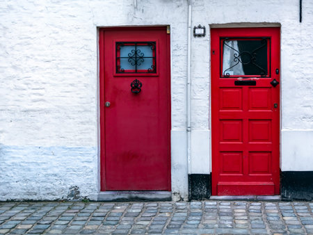 Two red wooden front doors in the white brick wall. Two vintage red doors with window at the top.の写真素材