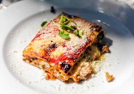 Lasagna with beef, tomatoes and eggplant, powdered with mozzarella. Restaurant serving. Lasagna on white plate.の写真素材