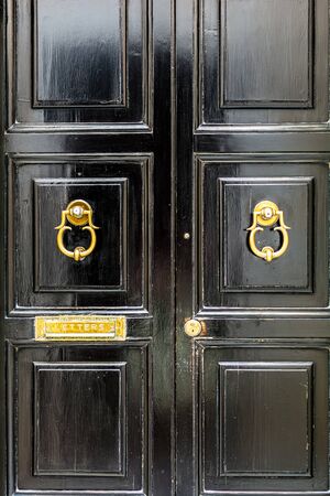 Black wooden door with golden vintage ornately shaped ring knockers and mail slot letterbox. Black door with golden hardware.の写真素材