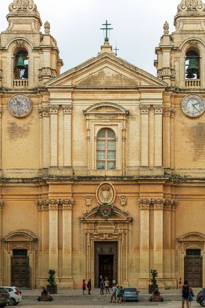 Mdina, Malta - August 31, 2019: Tourists before the entrance to St Paul's Cathedral. Divided into three bays by pilasters, the cathedral rises on three steps from the St. Paul's Square.のeditorial素材