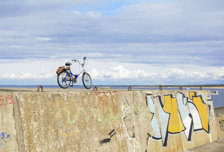 Riga, Latvia - April 26, 2020: Lonely bicycle standing at top of Mangalsala mole above white and yellow graffiti.のeditorial素材