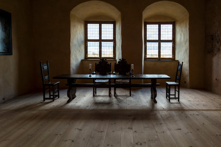 Bauska, Latvia - November 22, 2020: Interiors of Bauska Castle Duke's Residence - room with dark wooden table and four carved chair, two stained-glass windows and two large candles on the table.のeditorial素材