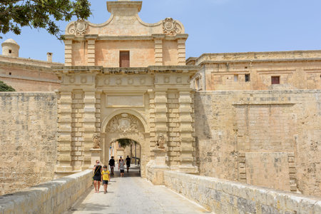 Mdina, Malta - June 29, 2021: Tourists walking through Baroque portal of Mdina Gate, also known as...