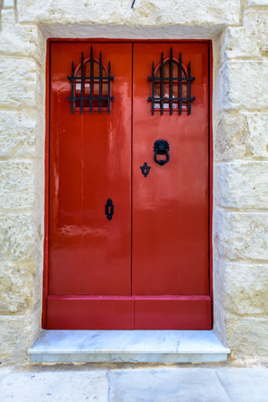 Red wooden door with black forged vintage lion head shaped ring knocker and gratings on small windows. Crimson door with black forged hardware.の写真素材