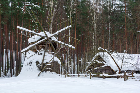 Old wooden log house and windmill covered with snow in a winter forest.の写真素材