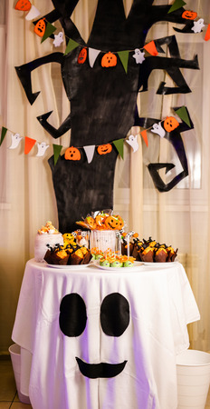 Candy bar with sweets for the celebration of Halloween. Huge black tree with decorations on the backgroundの写真素材