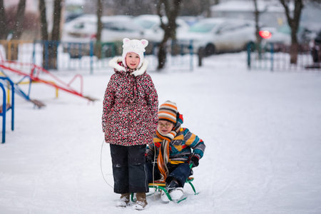 Boy and girl sledding in the snowy yard. Winter background.の写真素材