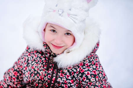 Smiling girl with white fur hat like a cat. Winter snowy background.の写真素材