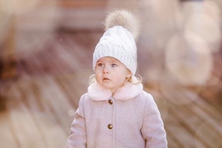 Portrait of cute little baby girl in pink coat and knitting hat with fur. Bokeh and unfocused snow on the background.の写真素材