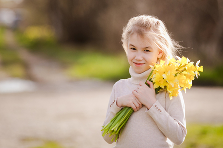 cute blonde happy little girl with yellow daffodils in the spring country.の写真素材