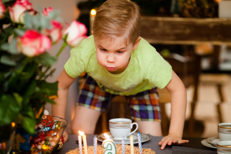 Beautiful adorable six year old boy in green shirt, celebrating his birthday, blowing candles on homemade baked cake, indoor.の写真素材