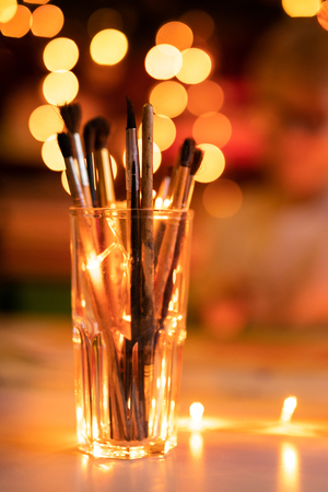 Glass with old artist brashes. Background with warm yellow bokeh. Christmas and New Year theme.の写真素材