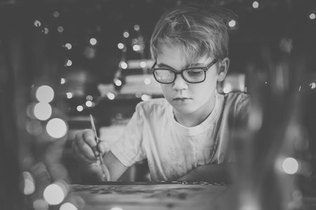 Blonde child boy writing letter to the Santa Claus or drawing something on the background with warm yellow bokeh. Christmas and New Year theme black and white.の写真素材