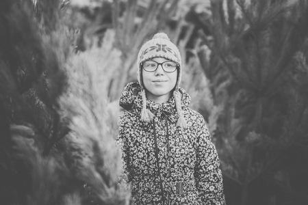 Girl with big glasses and gray and purple hat looking at green christmas tree. Black and white.の写真素材