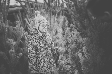 Girl with big glasses and gray and purple hat looking at green christmas tree. Black and white.の写真素材