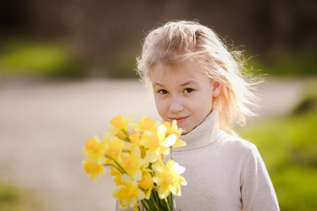 cute blonde happy little girl with yellow daffodils in the spring country.の写真素材