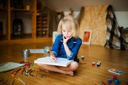 little blonde girl lying on the floor and drawing with colored pencilsの写真素材