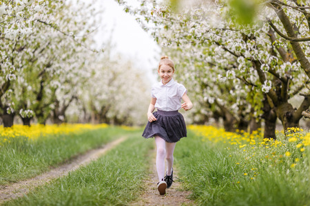 Little blonde girl running in blooming apple and cherry garden. Warm springtime and mothers and woman day.の写真素材