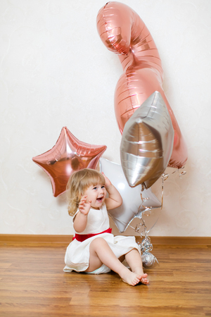 Little blonde baby girl two years old with big pink and white balloons on her birthday party.の写真素材