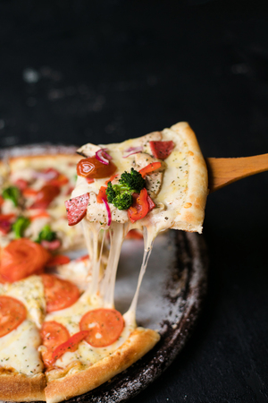 Tasty sliced pizza with basil leaves on black table.の写真素材