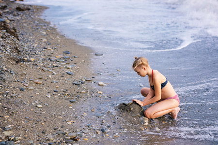 Having fun and joy concept. Blonde lovely girl with two braids playing with sea sand. Playful active...