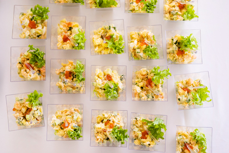 Little glasses with fresh salads, eggs, salmon and cucumbers standing on white table.の写真素材