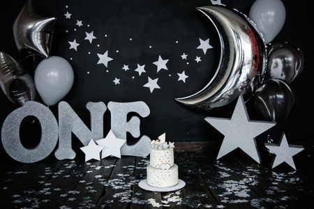 First birthday white cake with stars and candle for little baby boy and decorations for cake smash. Big silver letters ONE, silver stars and different balloons.の写真素材