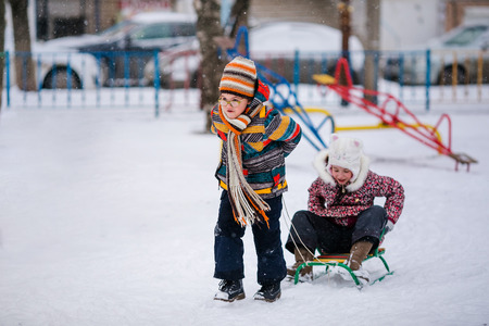 Boy and girl sledding in the snowy yard. Winter background.の写真素材