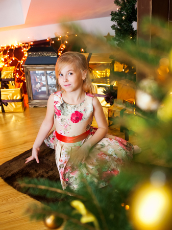 Little Blonde girl siting near the fireplace and Christmas tree.の写真素材